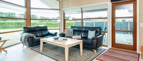 A spacious living area with two leather sofas, a wooden coffee table, and a large sliding glass door leading to an outdoor patio.