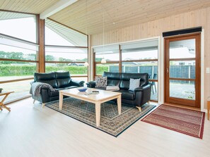 A spacious living area with two leather sofas, a wooden coffee table, and a large sliding glass door leading to an outdoor patio. - Holiday Home in Ansager (Ansager)