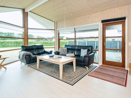 Amplia sala de estar con dos sofás de cuero, una mesa de centro de madera y un gran ventanal corredero que da a un patio exterior.