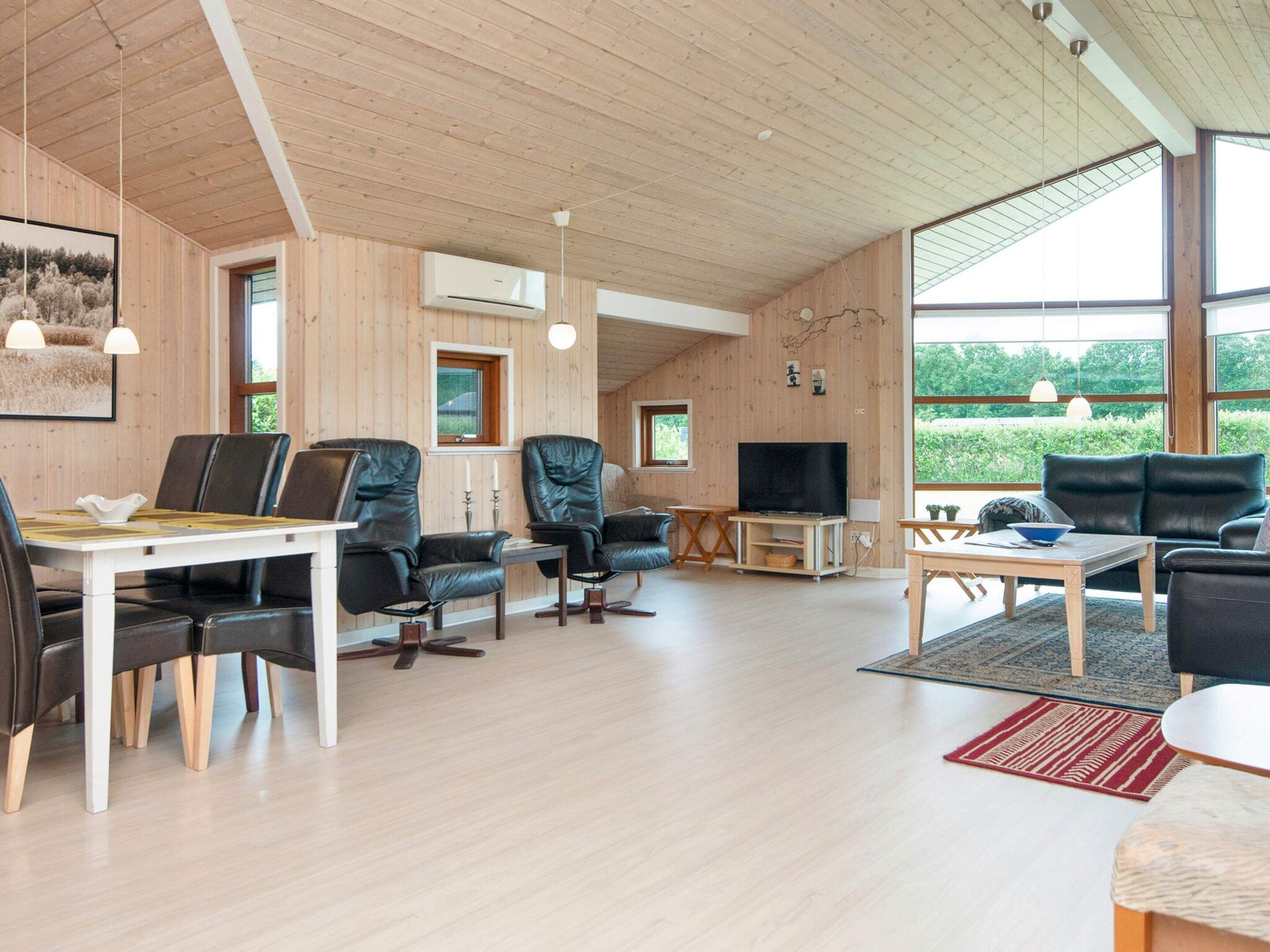 A modern living room with a dining area, wooden walls, and large windows.