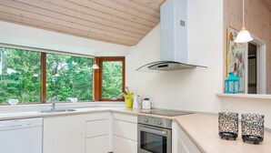 A modern kitchen with white cabinets, a stainless steel oven, and a large window offering a view of greenery. - Holiday Home in Ansager (Ansager)