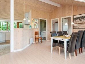 A modern interior with a wooden ceiling, a dining area with a white table and leather chairs, and a kitchen with white cabinets. - Holiday Home in Ansager (Ansager)