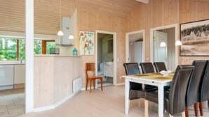 A modern kitchen with wooden walls, a dining area with a white table and black chairs, and a large framed picture on the wall. - Holiday Home in Ansager (Ansager)