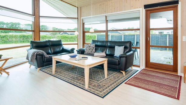 A modern living room with two black leather sofas, a wooden coffee table, and a large glass door leading to an outdoor area. - Holiday Home in Ansager (Ansager)