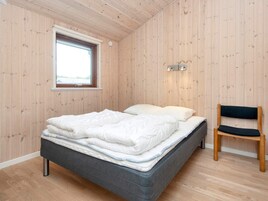 Un dormitorio con cama, una silla y ventana.