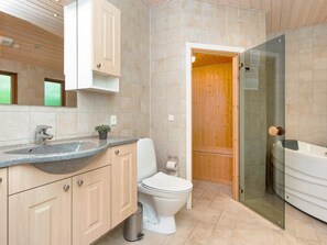Un baño moderno con lavamanos de granito, armarios de madera, inodoro y zona de ducha con mampara de vidrio.