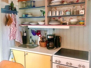A kitchen with a sink, stove, shelves with dishes, and a coffee maker.