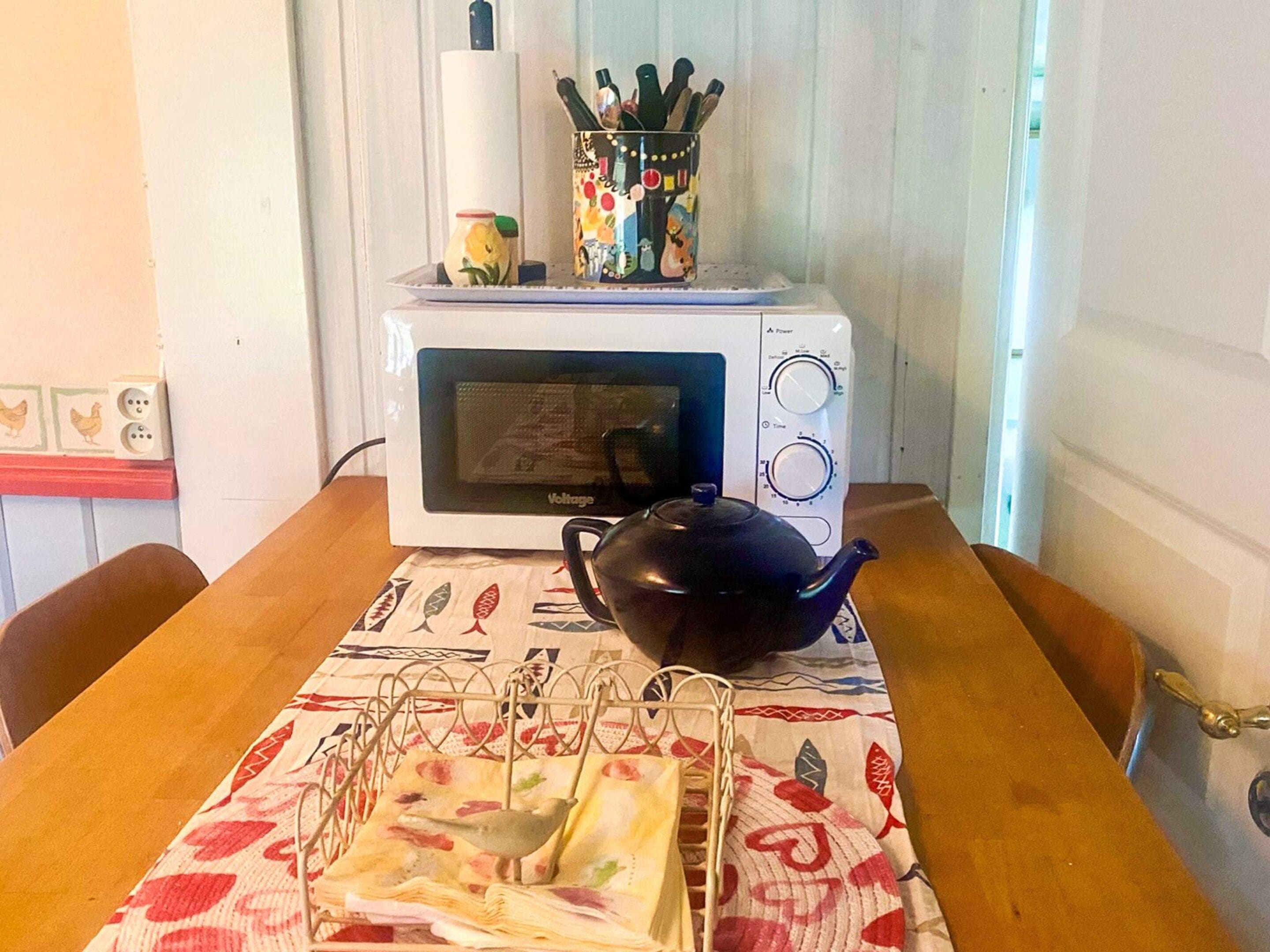 A microwave oven on a table with a teapot and a cloth napkin holder.