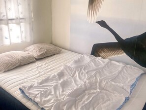 A bedroom with a bed, pillows, a window with curtains, and a wall with a partial view of a bird.