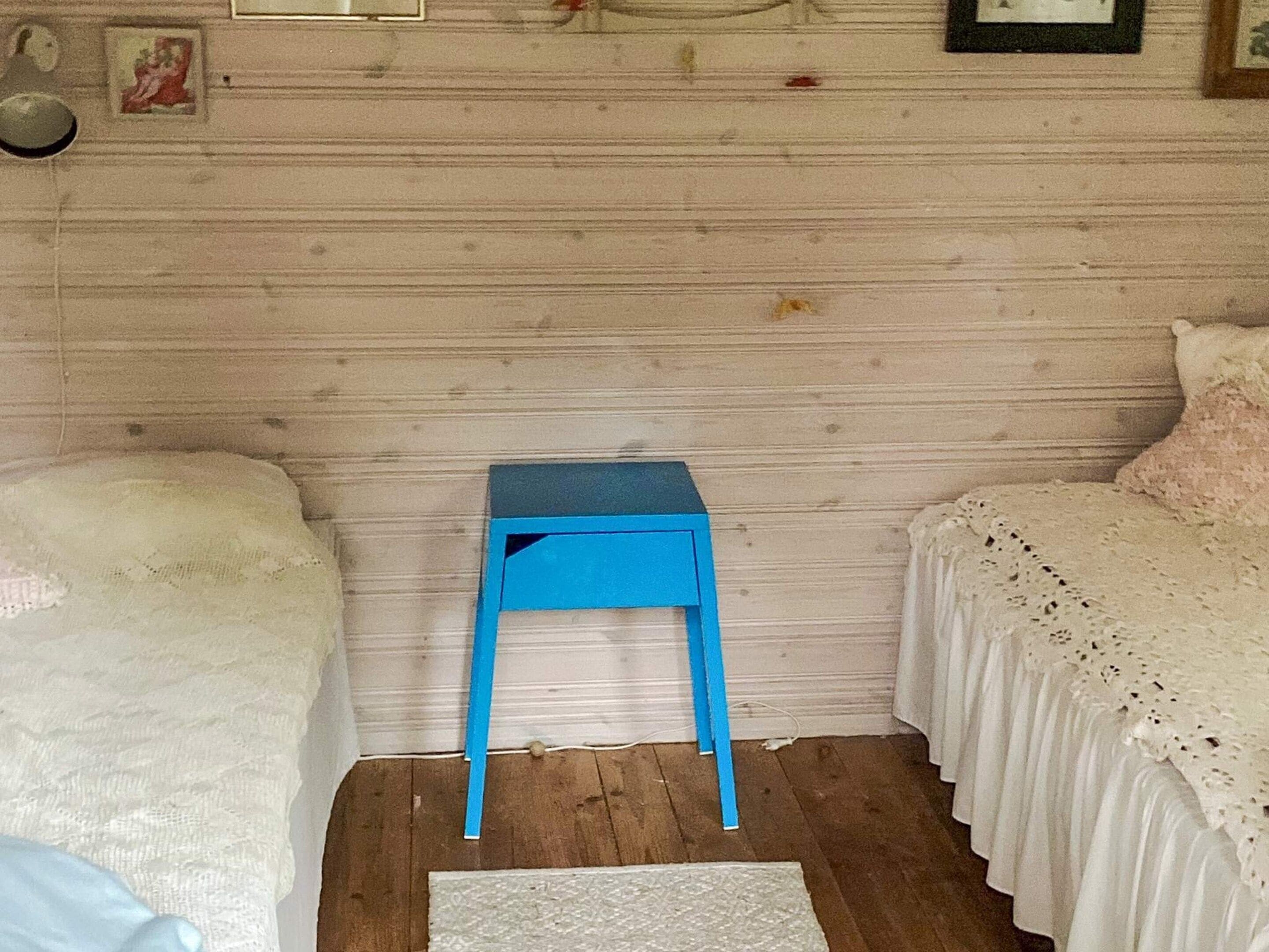 Un dormitorio con dos camas, una mesita de noche azul y una alfombra blanca.