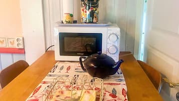A microwave oven on a table with a teapot and a cloth.
