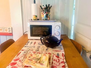 Een magnetron op een tafel, samen met een theepot en een doek.