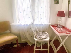A room with a window, a chair, a table with a lamp, and a radiator.