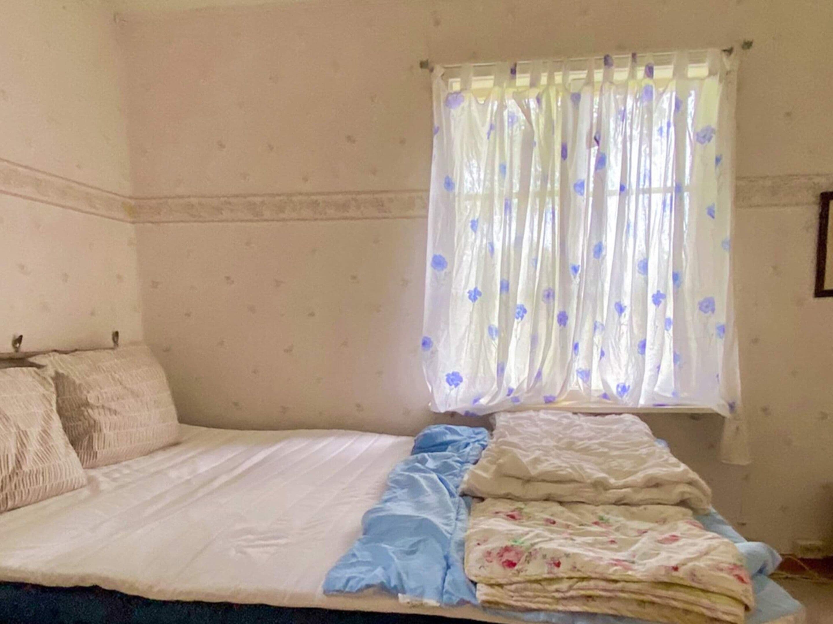 Een slaapkamer met een bed, kussens, een raam met gordijn en een bloemen behang.