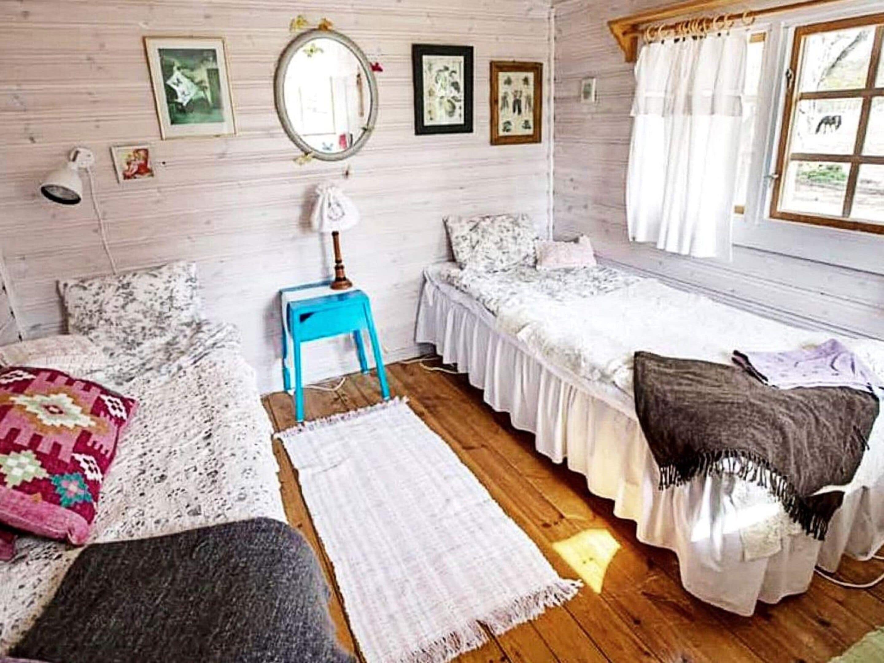 A room with two beds, a small table, a mirror, and artwork on the walls.