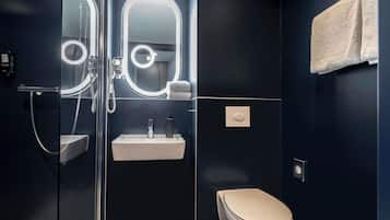 Un baño moderno con ducha envuelta en vidrio, un lavamanos blanco y un inodoro.