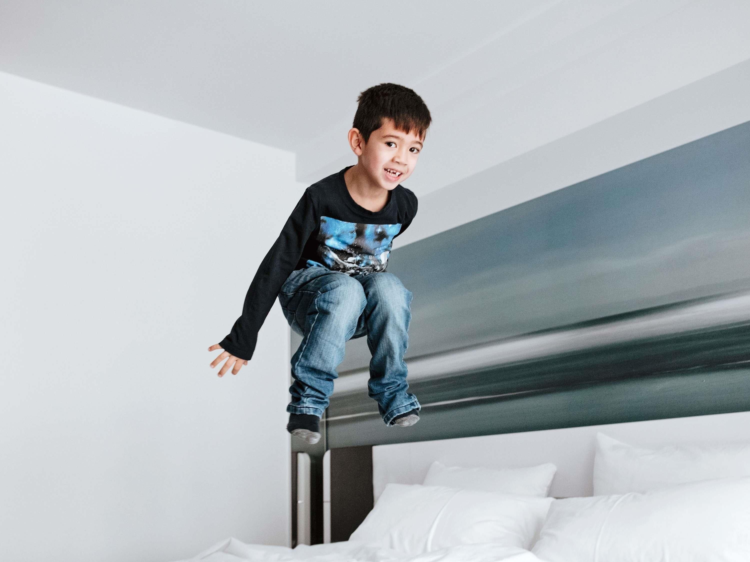 A child jumping off a bunk bed in a modern hotel room with white bedding and a minimalist design.