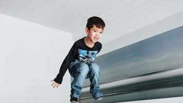 A child jumping off a bunk bed in a modern hotel room with white bedding and a minimalist design.