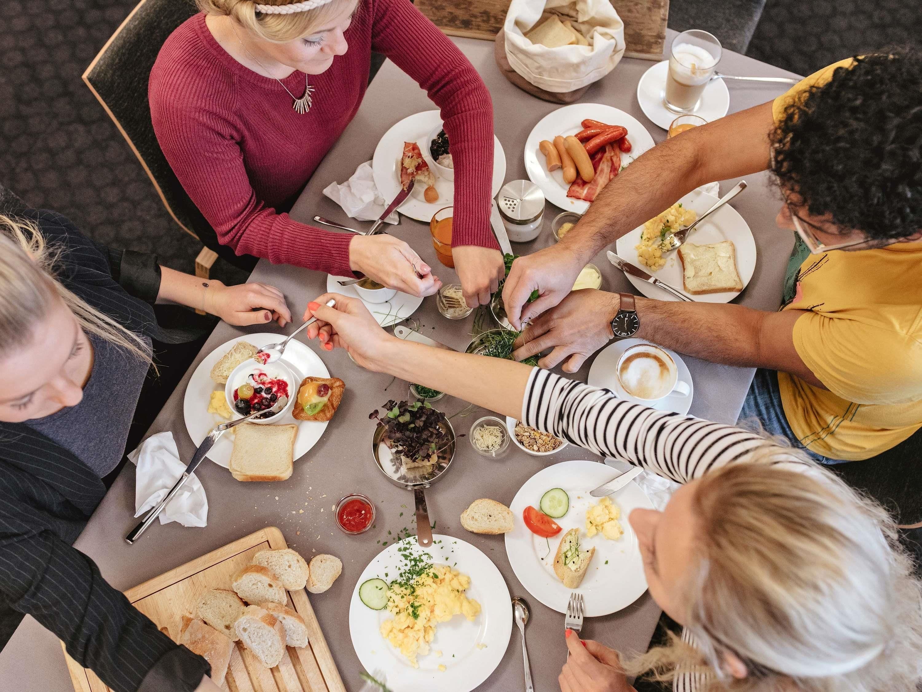 Un grupo de personas cenando en una mesa con diferentes platos, cubiertos y una cesta de pan.