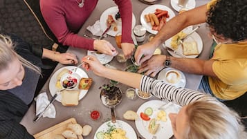 Un grupo de personas cenando en una mesa con diferentes platos, cubiertos y una cesta de pan.