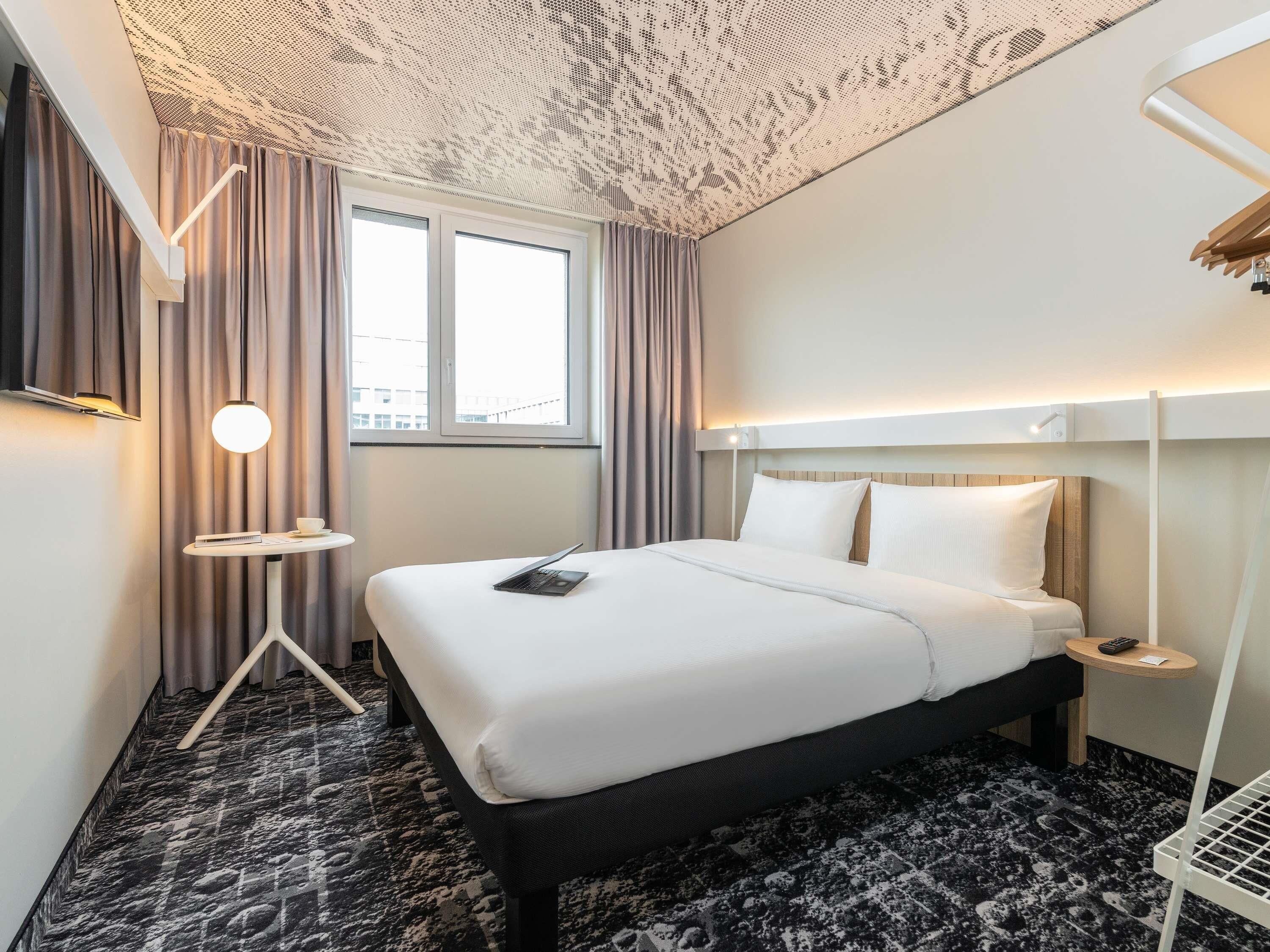 Ein Hotelzimmer mit Bett, Schreibtisch, Stuhl, Fenster und einer Decke mit einem besonderen Muster.