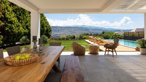 An outdoor patio with a wooden table, wicker chairs, and a view of mountains. - Luxury Ensuite Villa Overlooking Souda Bay (Chania)