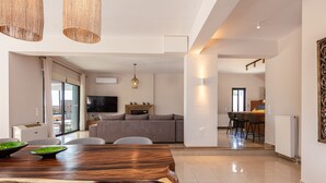 A modern living space with a dining area, kitchen, and a seating area with a TV. - Luxury Ensuite Villa Overlooking Souda Bay (Chania)