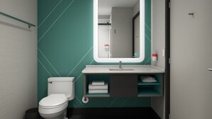 A modern bathroom with a white toilet, a teal accent wall, a white sink with a mirror, and a towel rack. - avid hotel Cincinnati N - West Chester by IHG (West Chester)