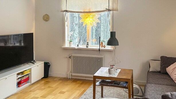 A living room with a TV, a radiator, a window with a view of trees, a table with a lamp, and a sofa. - 7 Person Holiday Home in Docksta (Docksta)