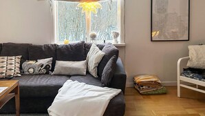 A living room with a dark grey sofa, a white throw blanket, and a window with a view of trees. - 7 Person Holiday Home in Docksta (Docksta)