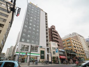A multi-story hotel with a prominent 'Super Hotel' sign, a variety of shops on the ground floor, and a busy street with vehicles and pedestrians. - Super Hotel Yokohama Kannai (Yokohama)