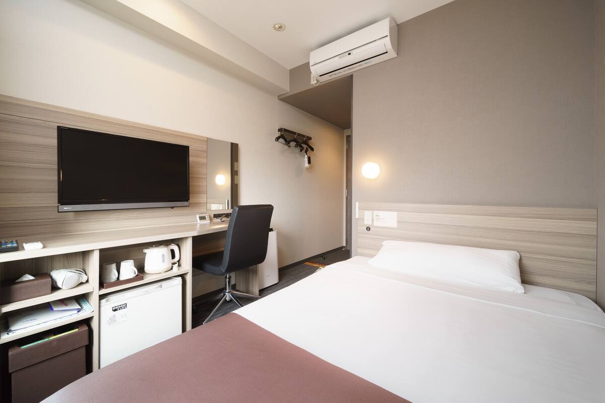 Ein Hotelzimmer mit Bett, Schreibtisch mit Stuhl, Fernseher, Minibar und Klimaanlage.