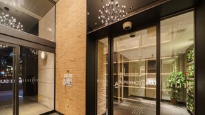 A hotel entrance with a glass door, a brick wall, and a security camera. - Super Hotel Yokohama Kannai (Yokohama)