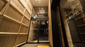 A hotel entrance with a modern design, featuring a glass door, a visible emergency exit sign, and a chandelier above the entrance. - Super Hotel Yokohama Kannai (Yokohama)
