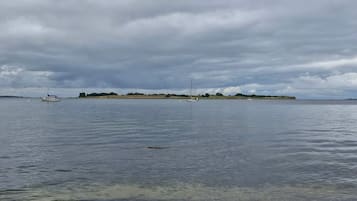 A calm body of water with boats and a distant landmass under a cloudy sky.