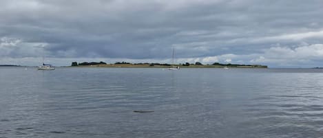 A calm body of water with boats and a distant landmass under a cloudy sky.