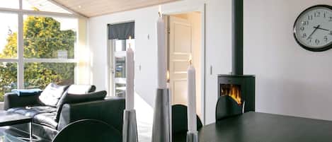 A modern living room with a fireplace, a clock on the wall, and a view of the outdoors.
