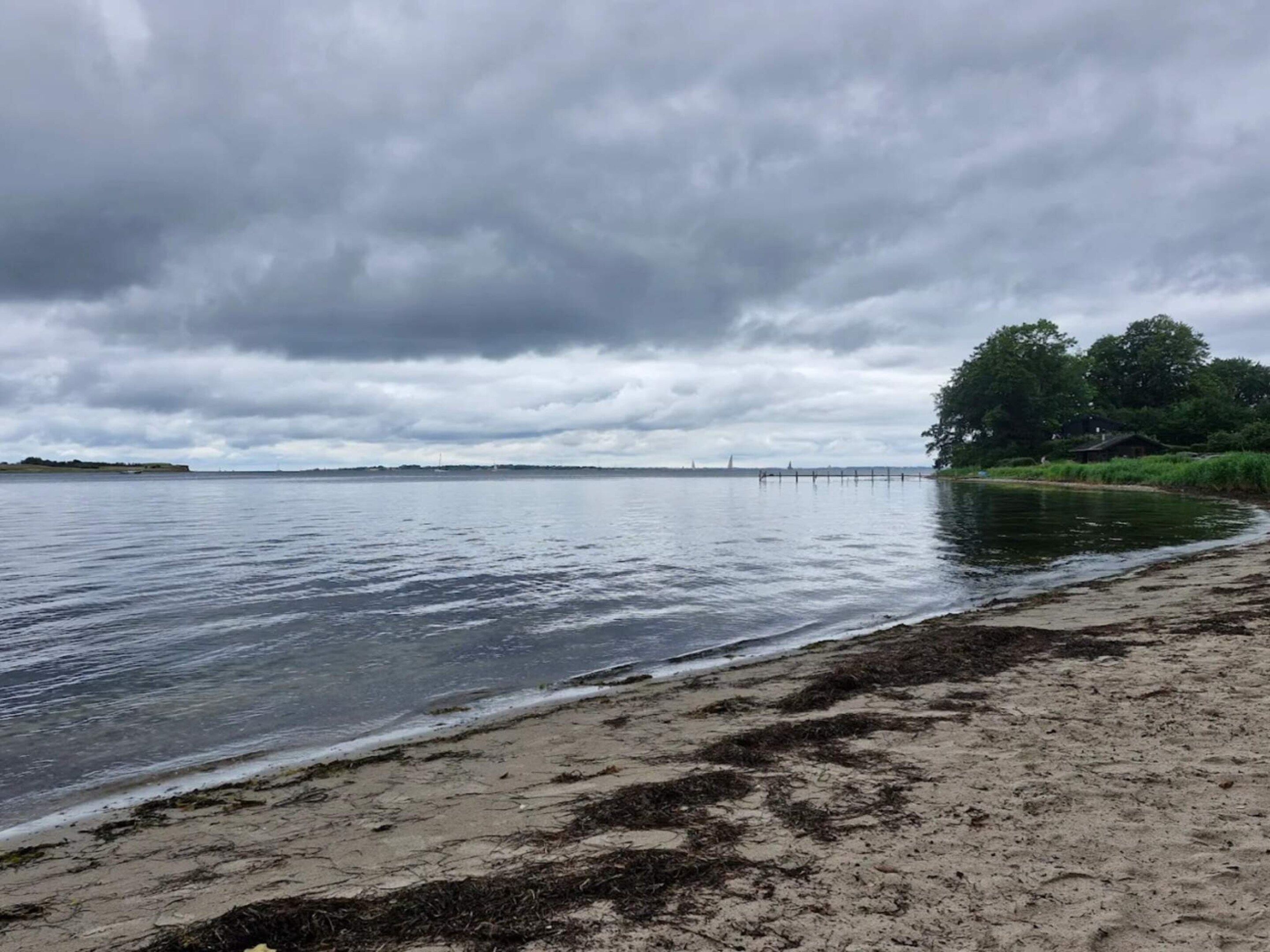 Een strand met een rustige zee, een zandstrand en een bewolkte lucht.