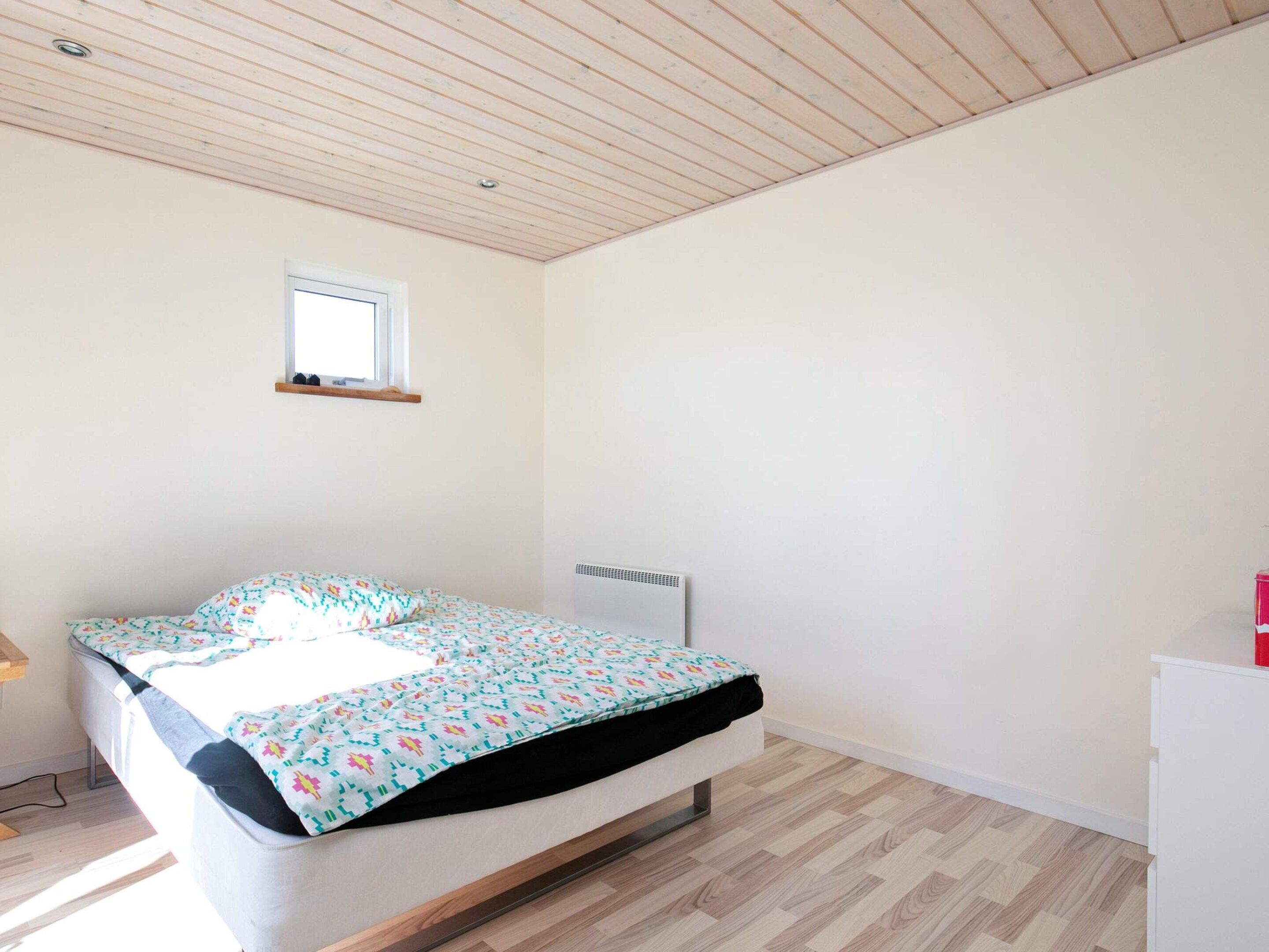 A bedroom with a bed, a window, a radiator, and a wooden floor.