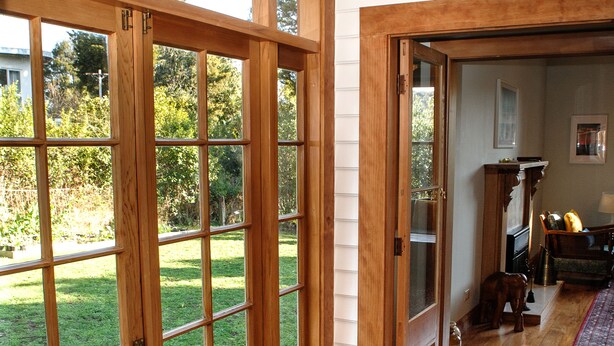 A room with a large sliding glass door leading to a backyard, a wooden floor, and a rug. - Elegant Villa Nestled In The Trees (Nelson)