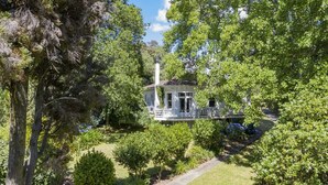 A white house with a porch, surrounded by lush greenery and trees. - Elegant Villa Nestled In The Trees (Nelson)