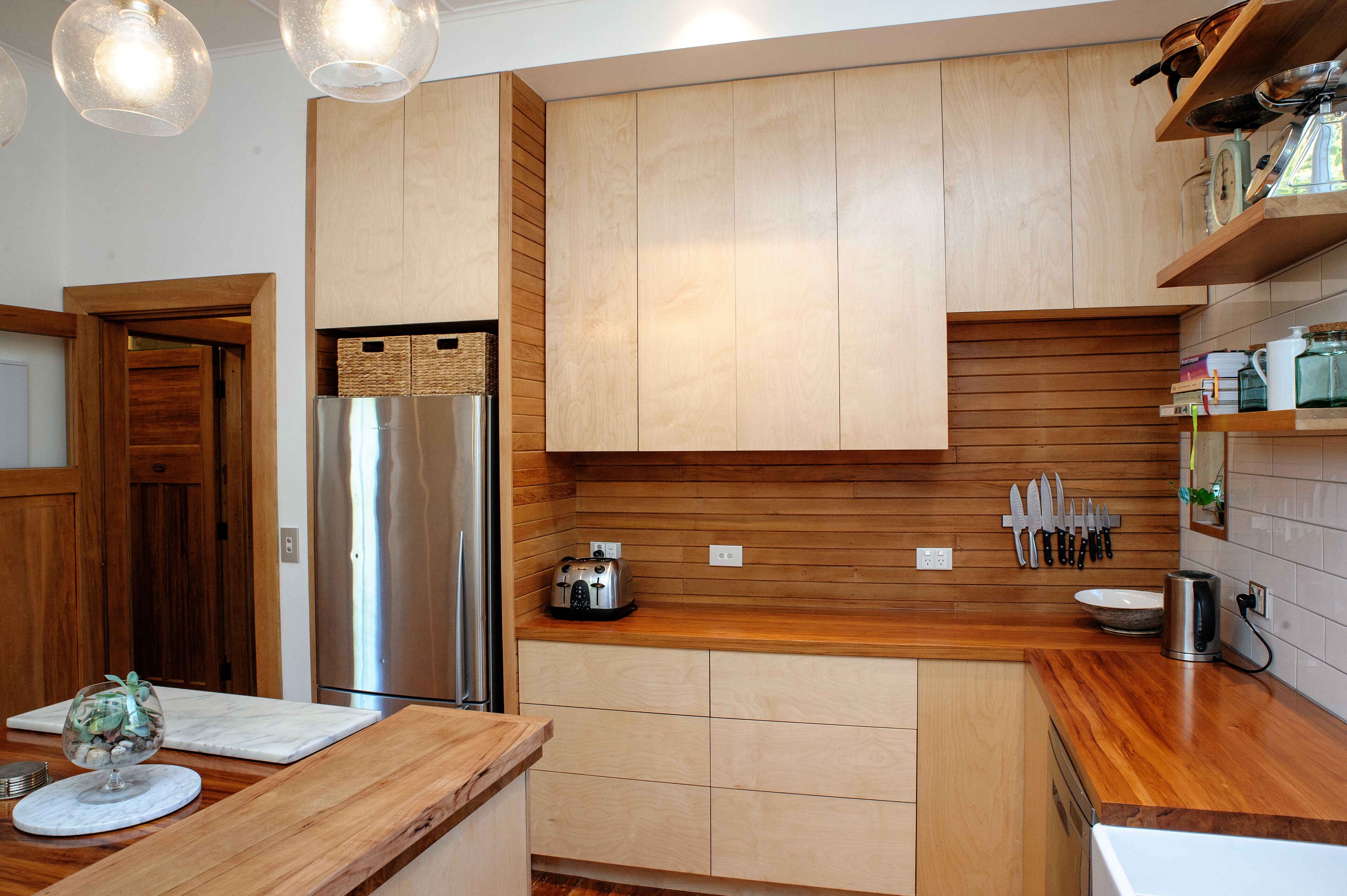 Une cuisine moderne avec des meubles en bois, un réfrigérateur en acier inoxydable, un grille-pain et un porte-couteaux.