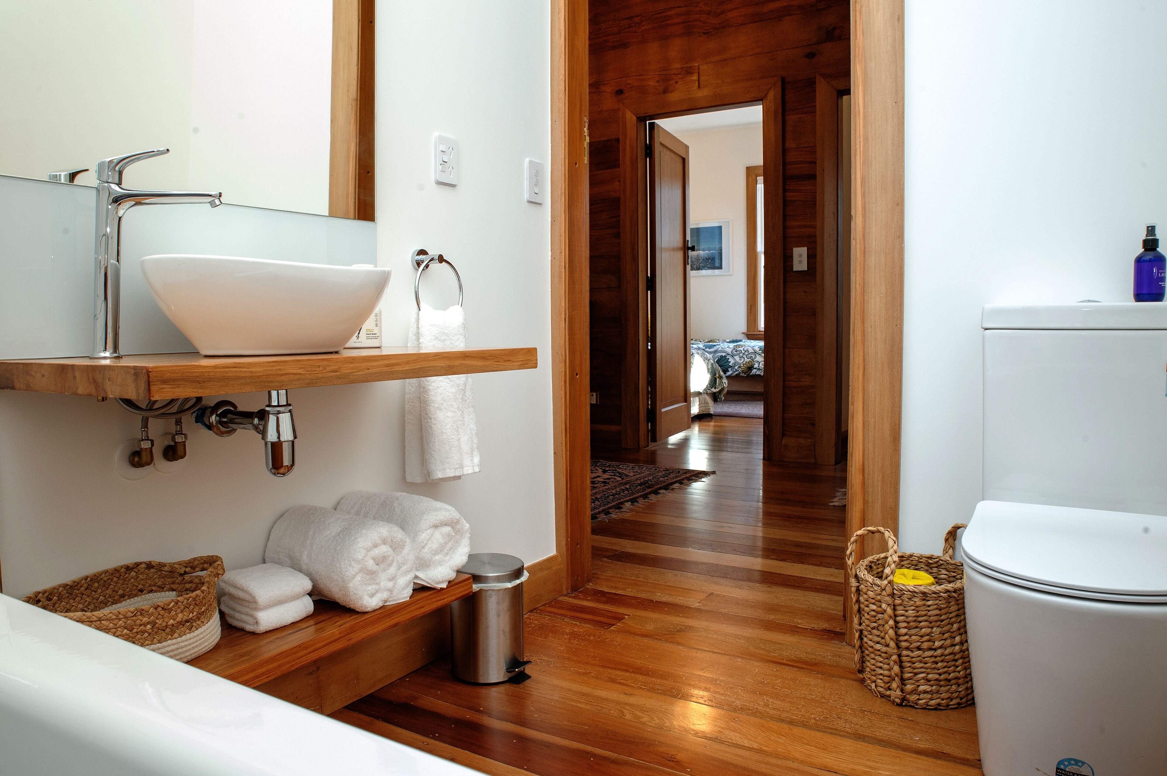 Ein Badezimmer mit einem weißen Waschbecken, einem Holzschrank und einer weißen Toilette. Auf dem Schrank liegen Handtücher und Körbe.