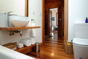 A bathroom with a white sink, wooden vanity, and a white toilet. There are towels and baskets on the vanity. - Elegant Villa Nestled In The Trees (Nelson)