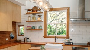 A modern kitchen with wooden countertops, a central island, and pendant lighting. - Elegant Villa Nestled In The Trees (Nelson)