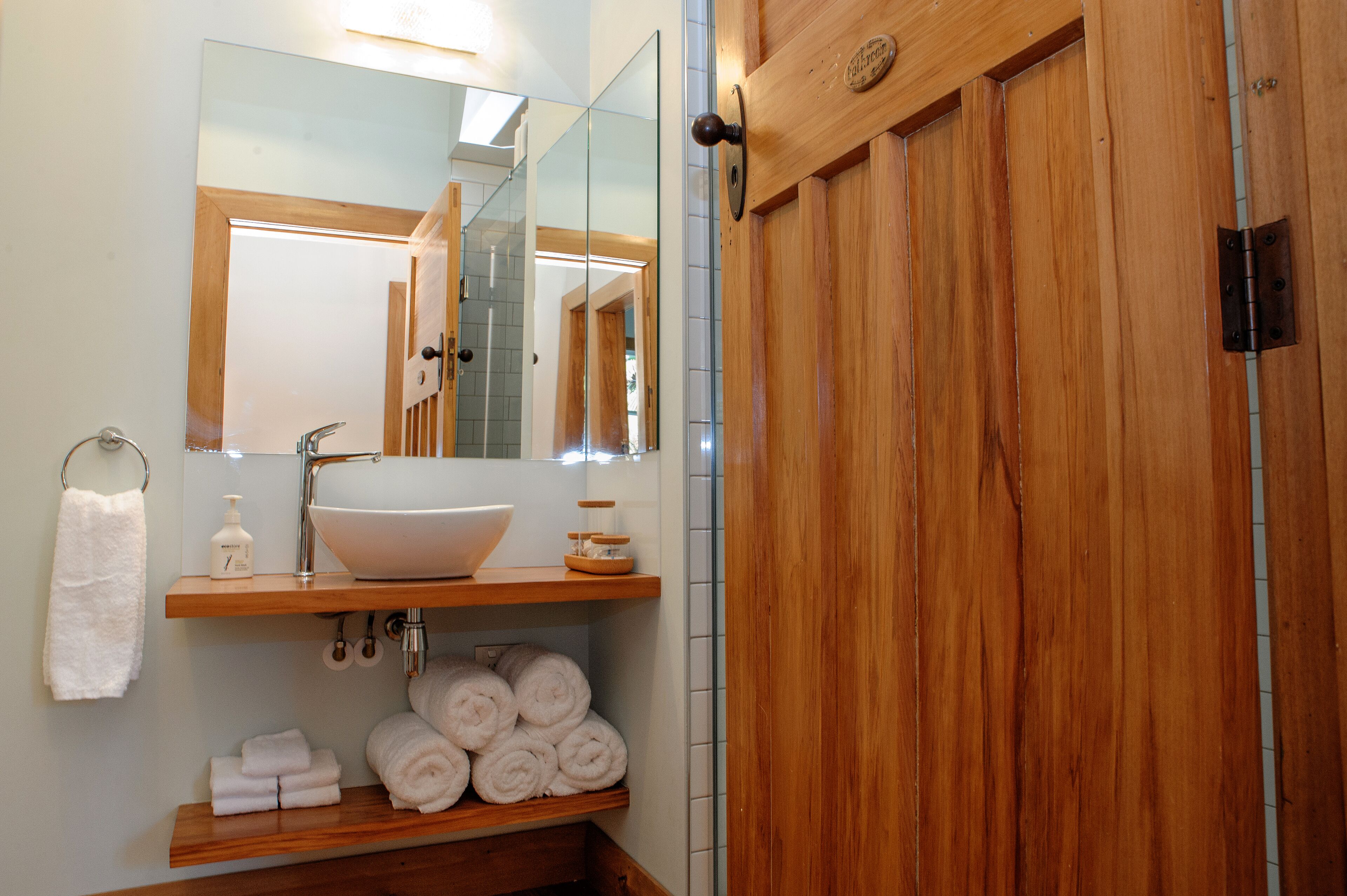 Un baño con tocador de madera, lavamanos blanco y espejo.