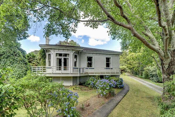 A two-story house with a covered porch, surrounded by lush greenery and a winding driveway. - Elegant Villa Nestled In The Trees (Nelson)