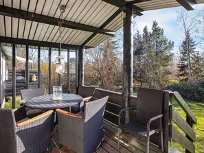 A covered outdoor seating area with wicker furniture and a table, overlooking a garden with trees and a wooden deck. - 7 Person Holiday Home in Vig (Vig)