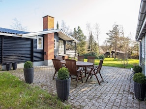 A patio area with a table and chairs, a brick chimney, and a wooden deck. - 7 Person Holiday Home in Vig (Vig)