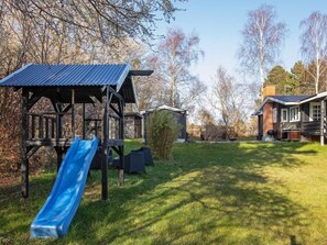 A wooden play structure with a slide, a small shed, and a house with a chimney.